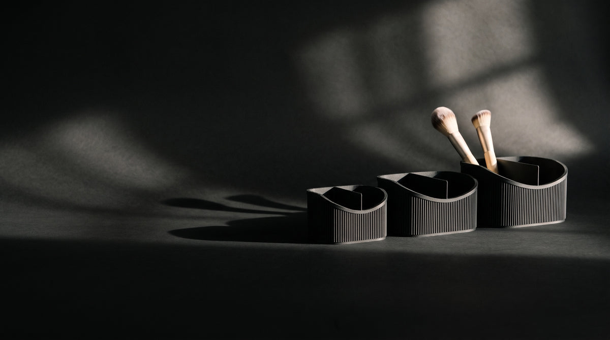 Three black ribbed vanity caddies under hard, low light on a dark studio sweep