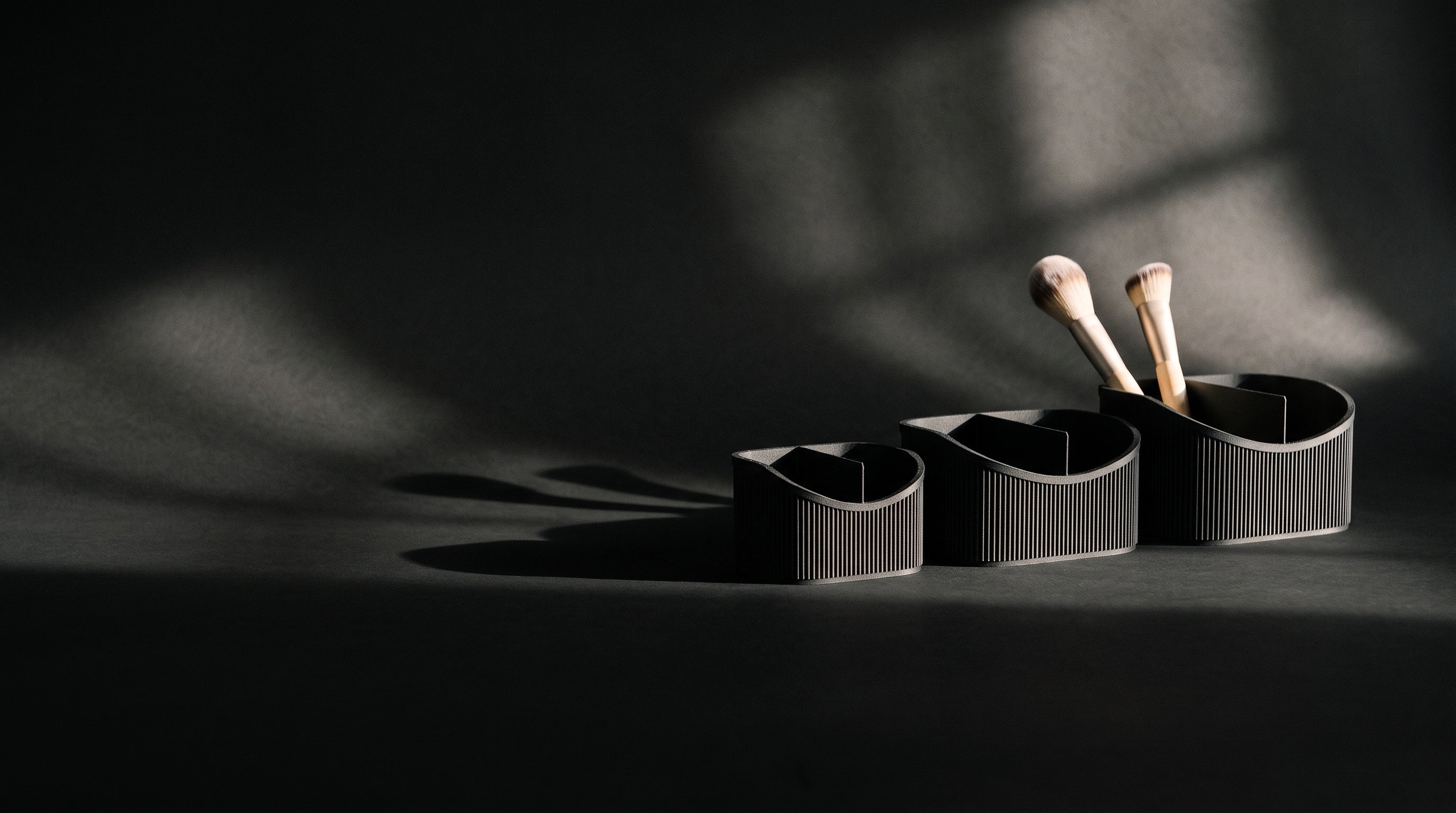 Three black ribbed vanity caddies under hard, low light on a dark studio sweep