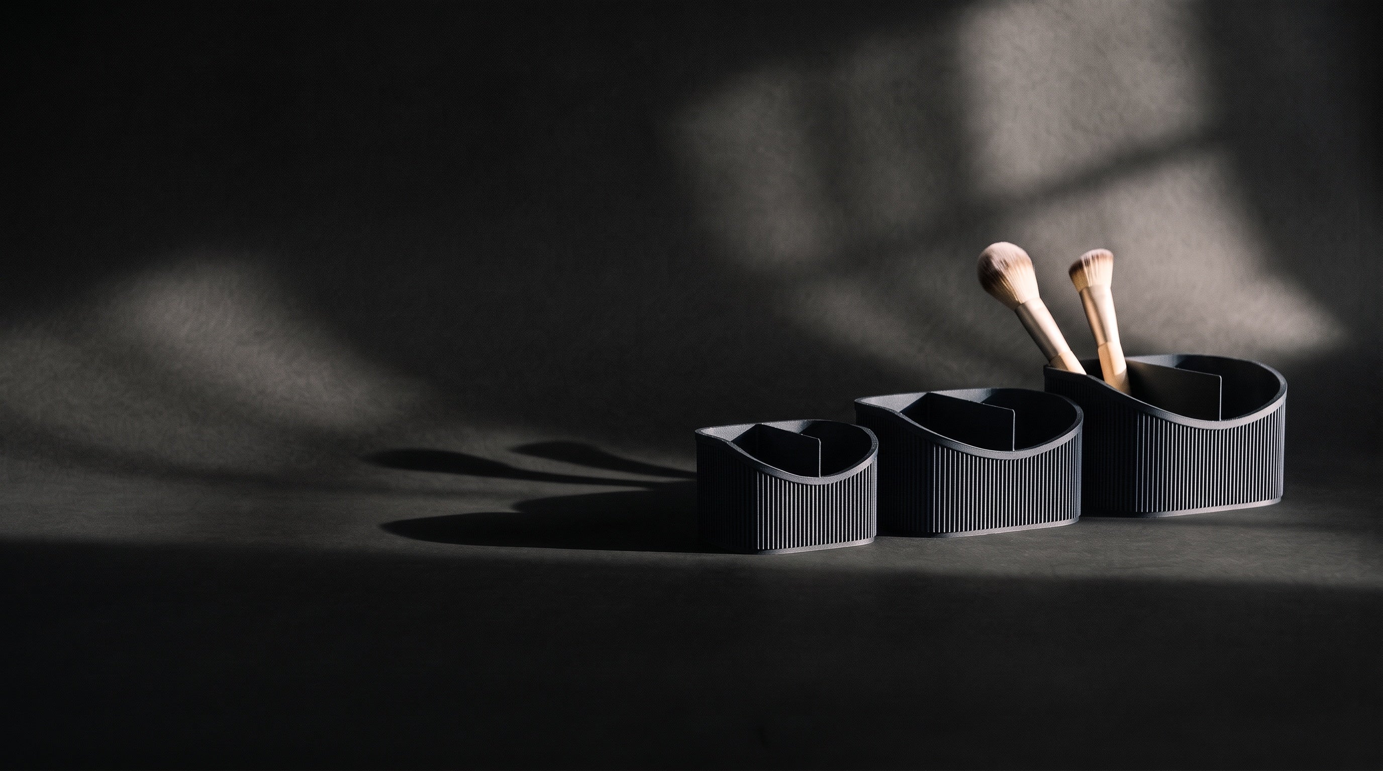 Three grey ribbed vanity caddies under hard, low light on a dark studio sweep
