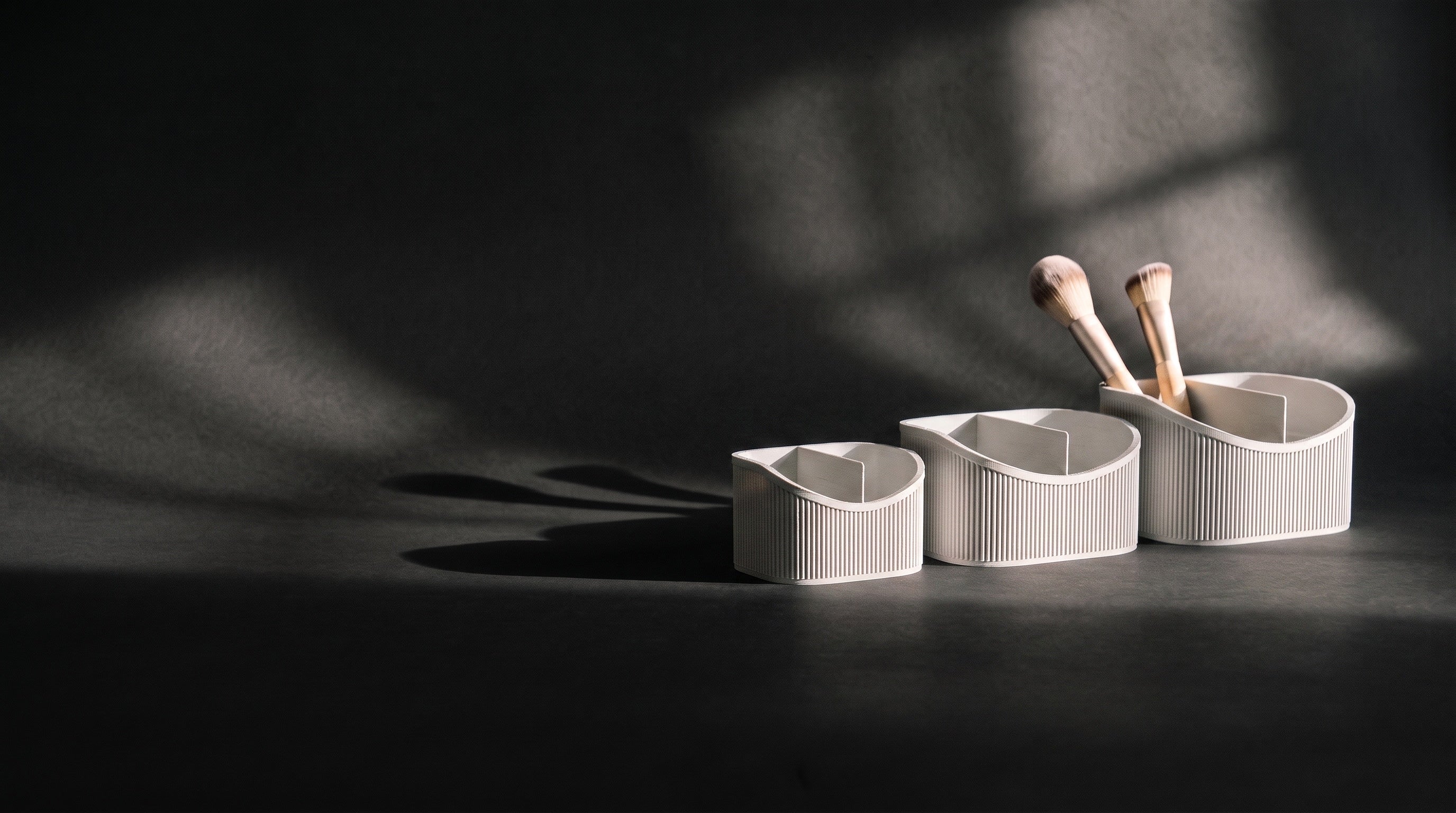 Three white ribbed vanity caddies under hard, low light on a dark studio sweep